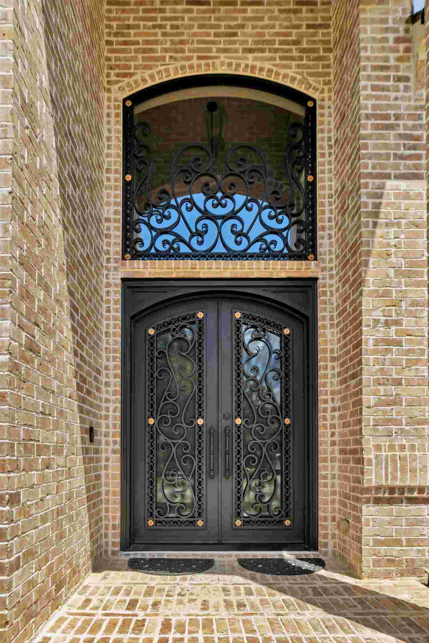 Iron double door with arched top, black finish, transom, scrollwork, and brass studs