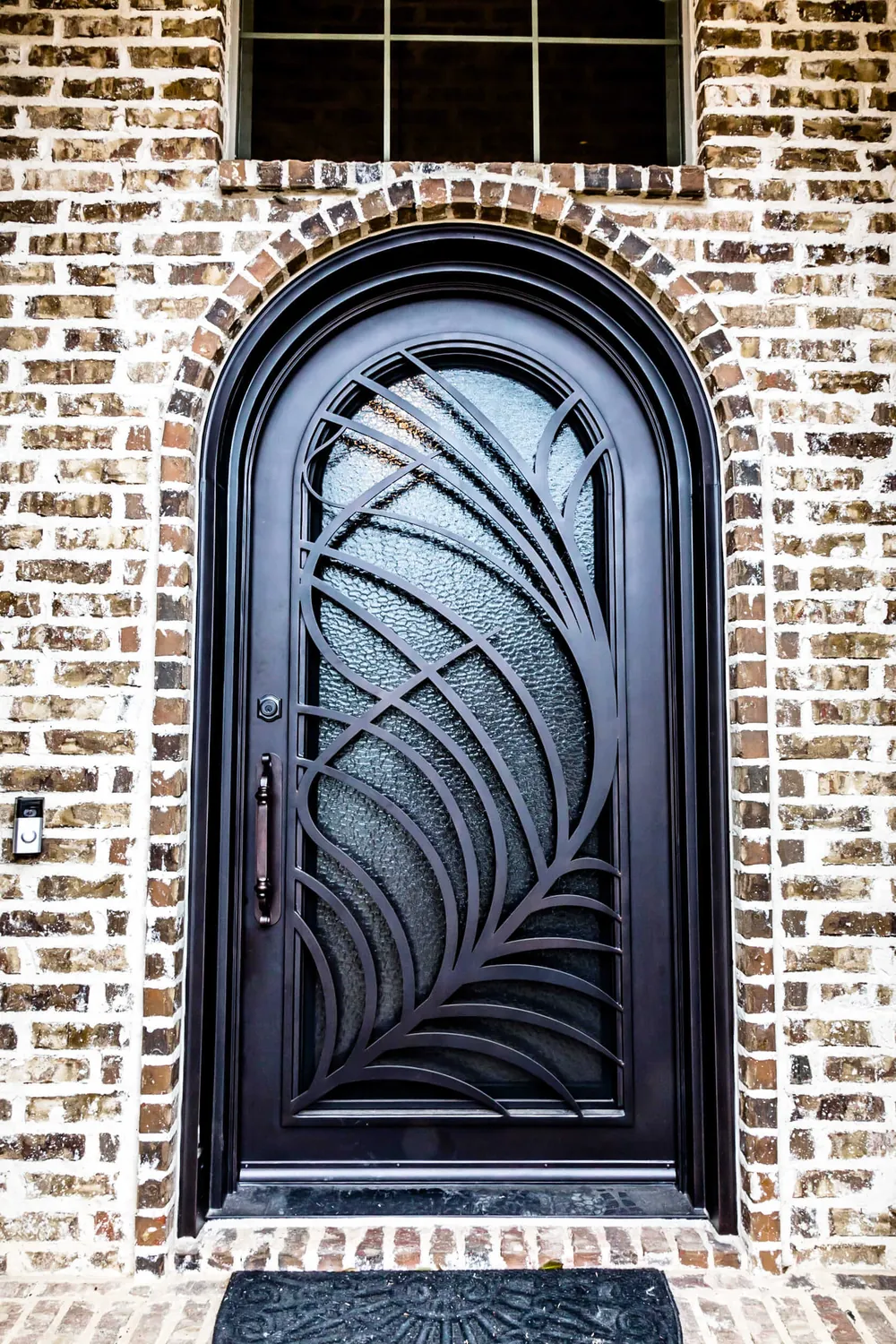 Arched steel entry door with decorative leaf design and textured glass in brick exterior - Love That Door
