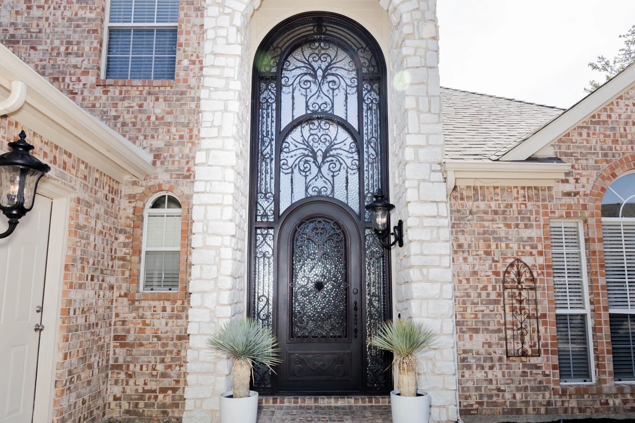 Black iron double arched entry door with scrollwork and clear glass, stone archway