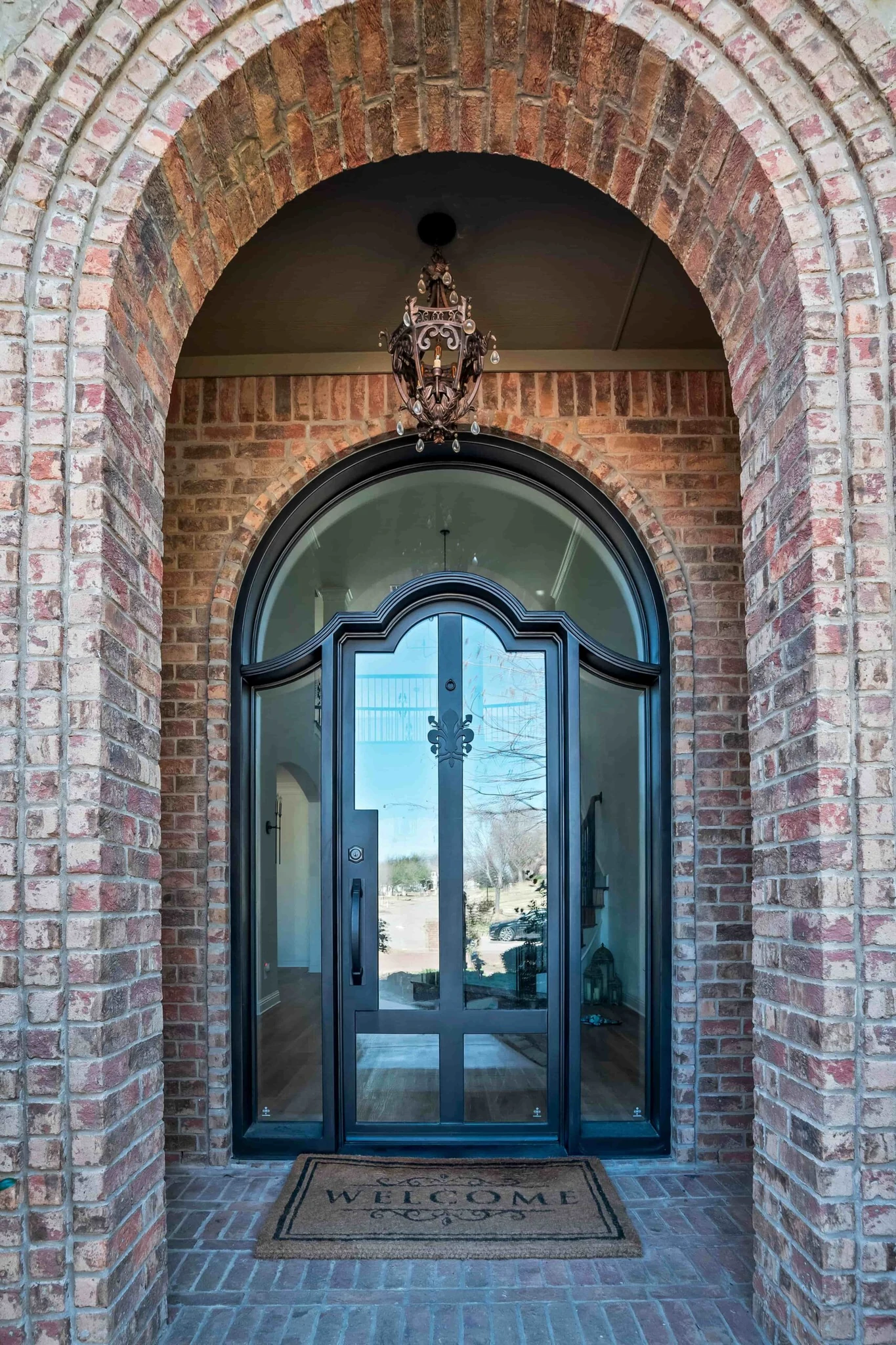 Black metal double arched entry door with scrollwork and clear glass, brick archway