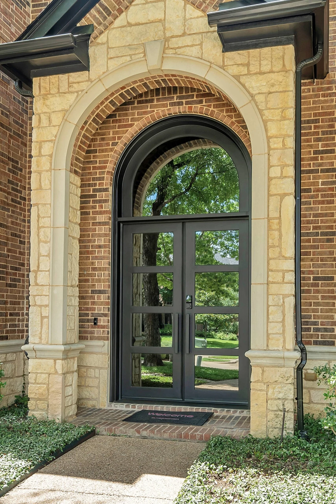 Black steel double rectangular entry door with large glass in arched stone frame