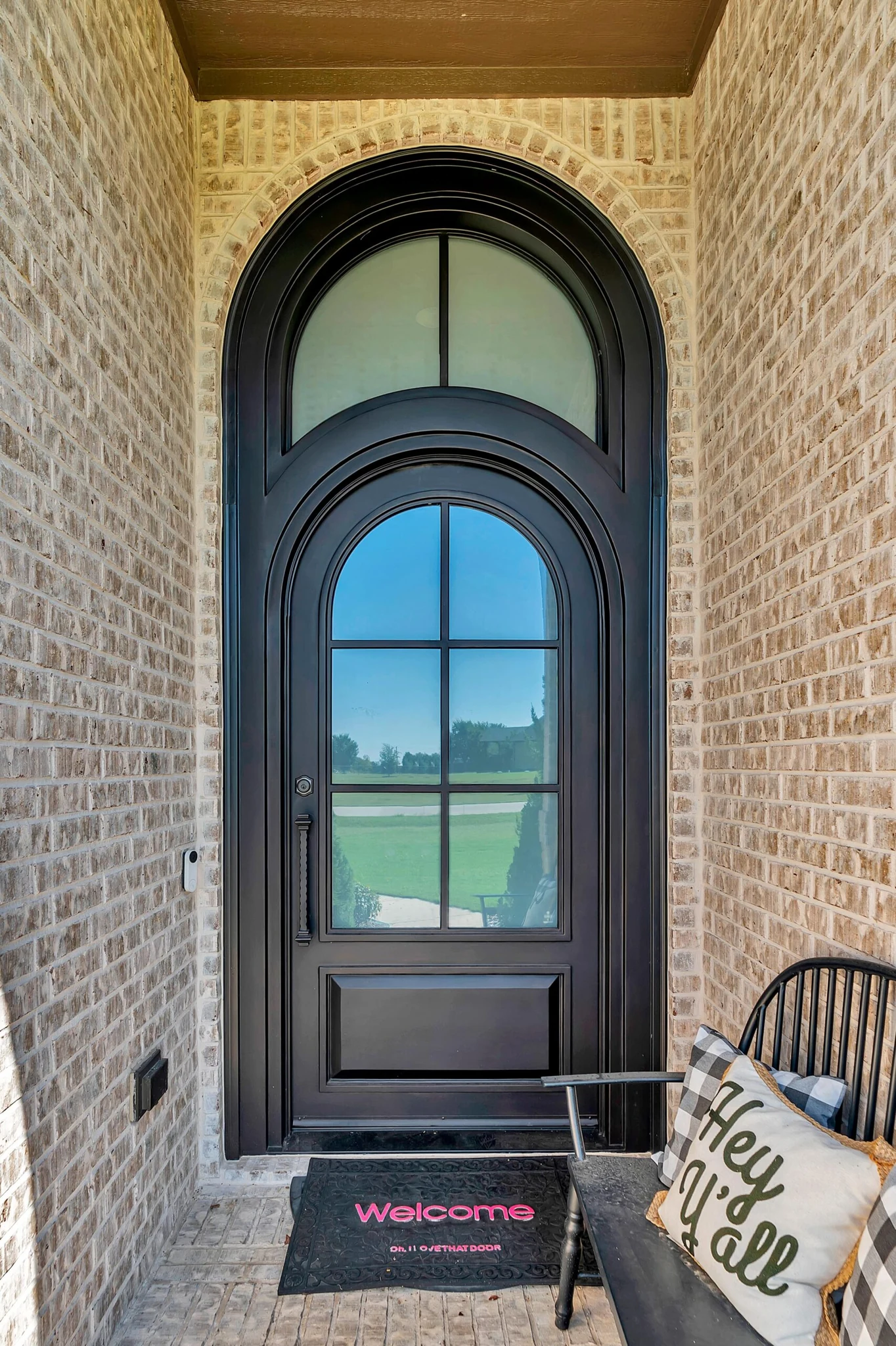 Black steel single arched entry door with grid glass, brick wall