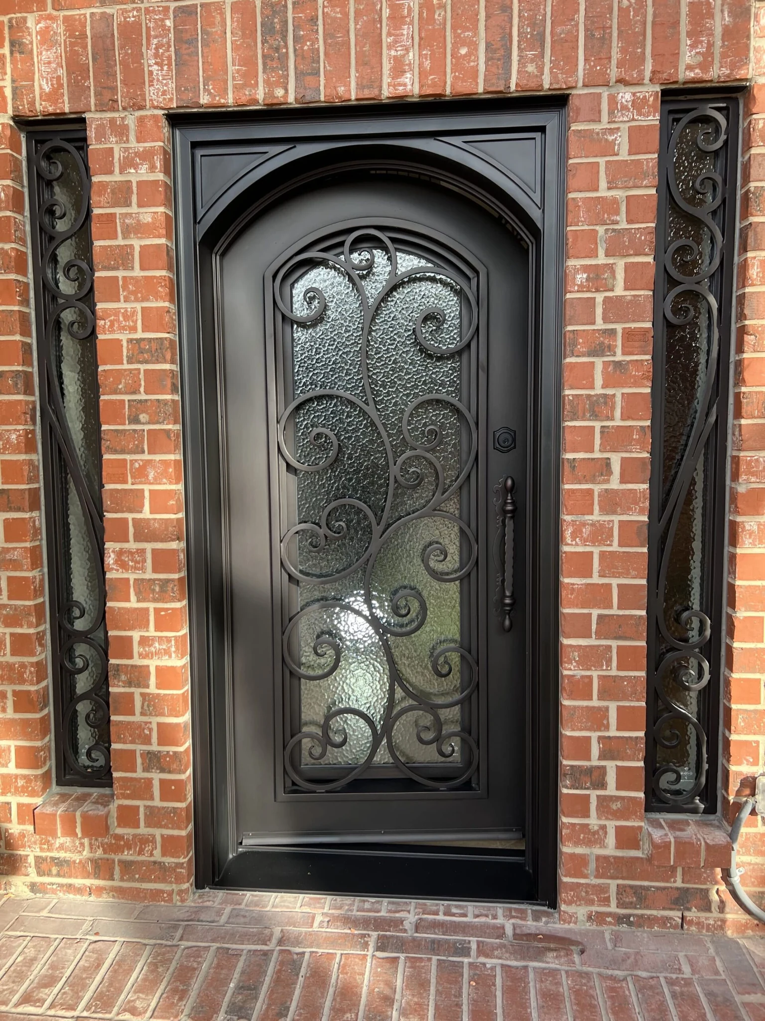 Black steel single arched entry door with scrollwork, textured glass and sidelights