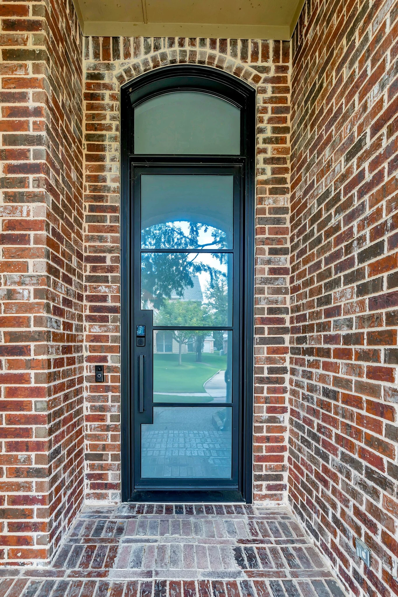 Black steel single rectangular entry door with transom, brick exterior