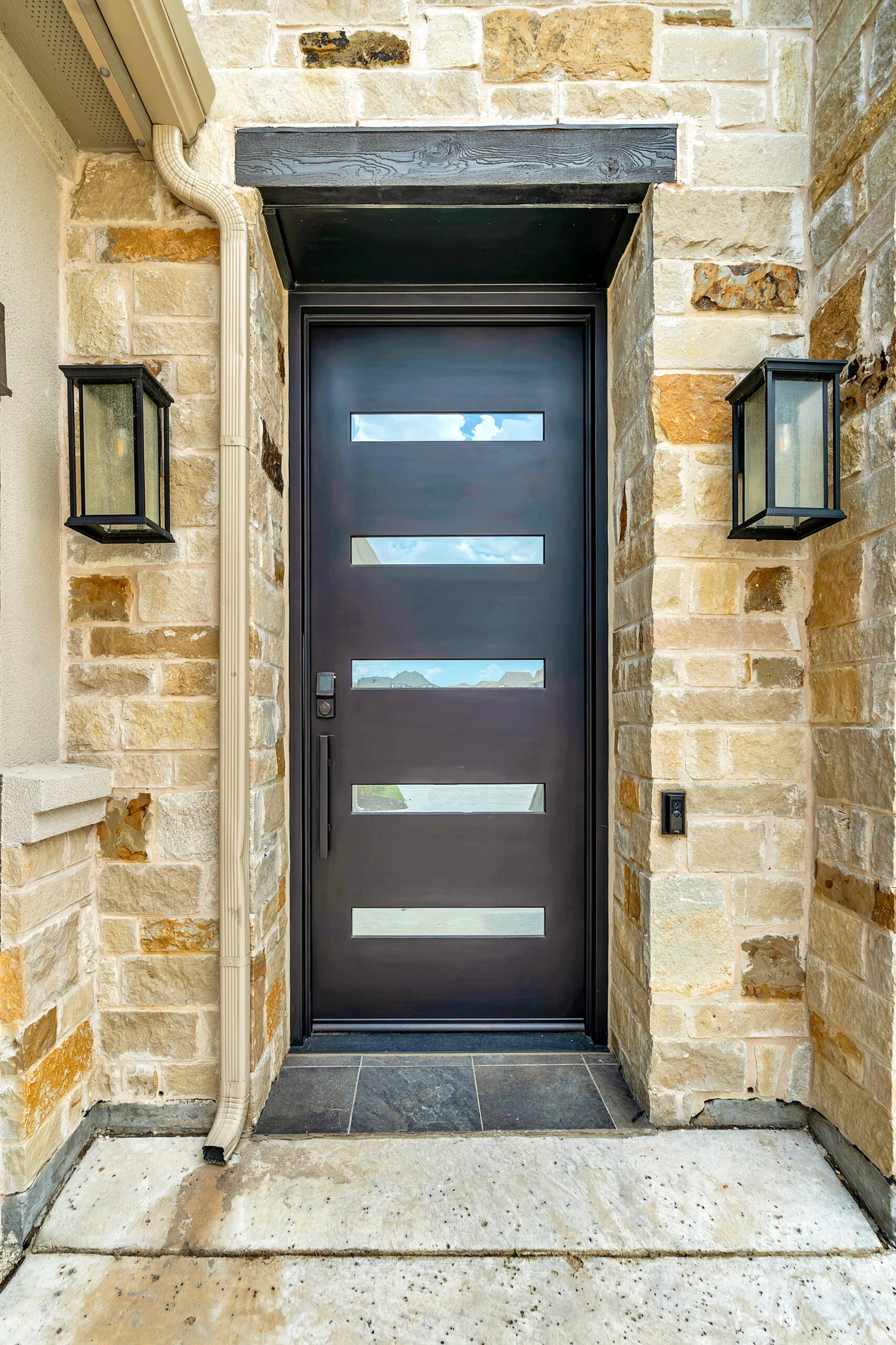 Dark bronze pivot door with horizontal glass panels against stone wall - Love That Door