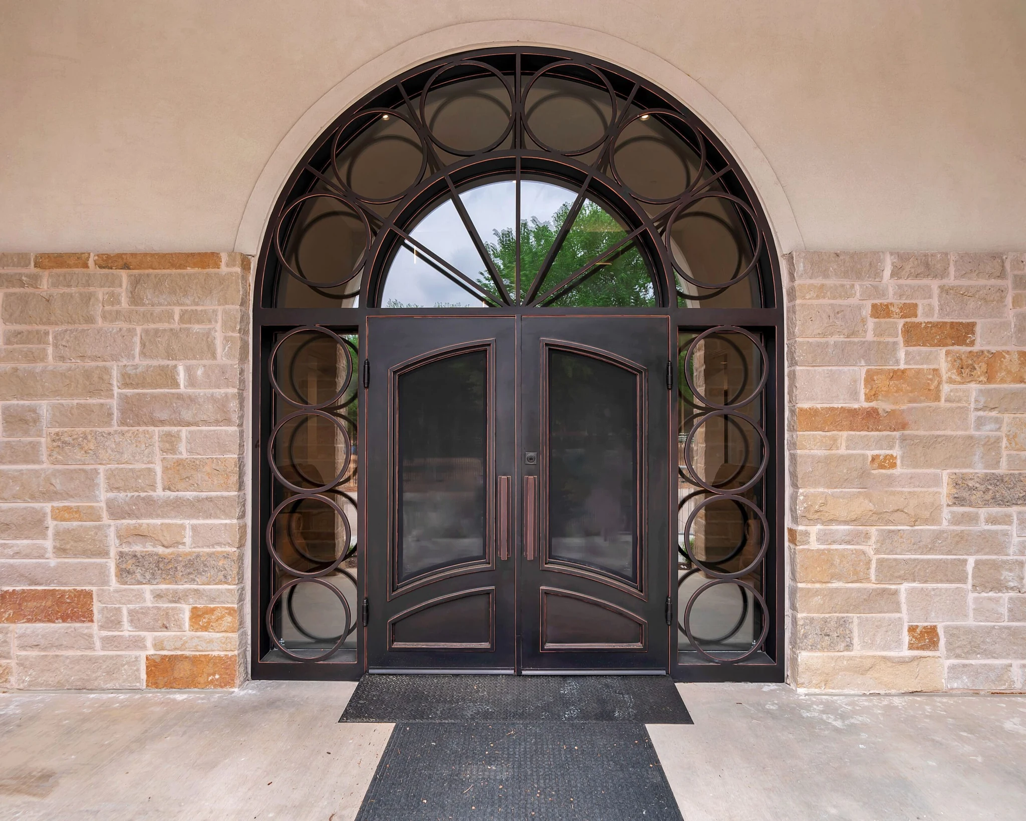 Dark bronze steel double arched entry door with circular glass, stone background