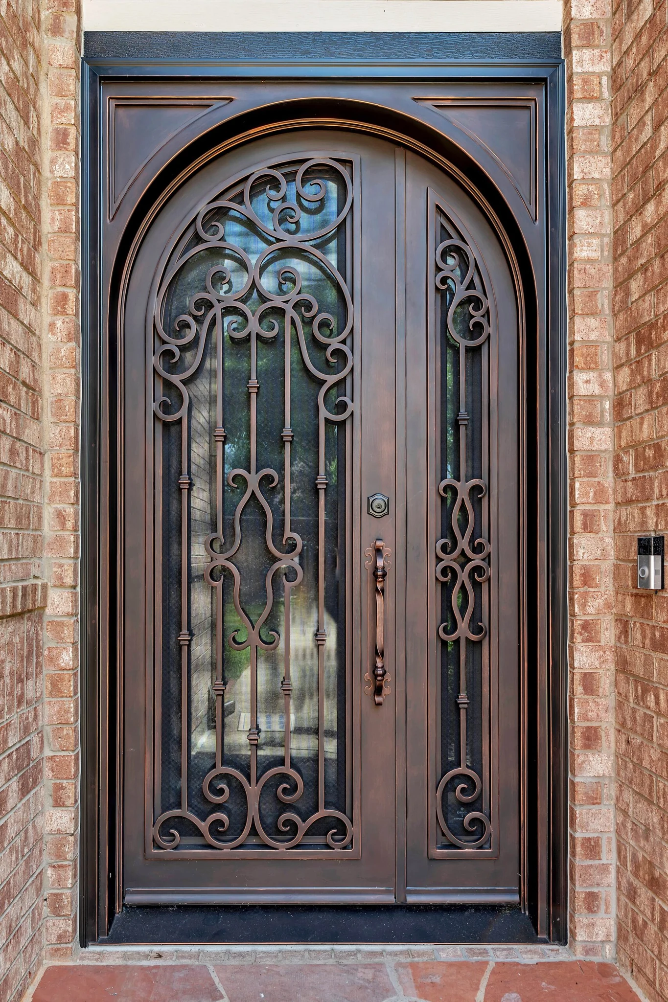 Dark bronze steel double arched entry door with scrollwork, brick exterior