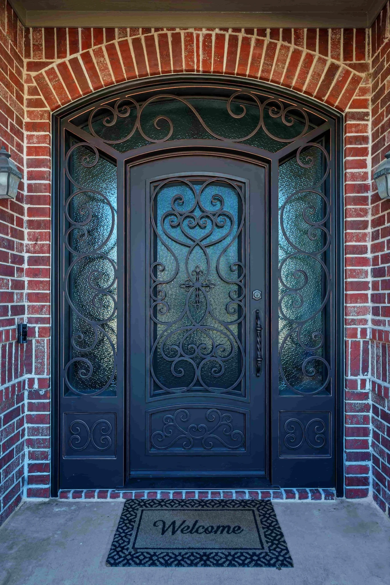 Dark steel double arched entry door with scrollwork and textured glass, brick