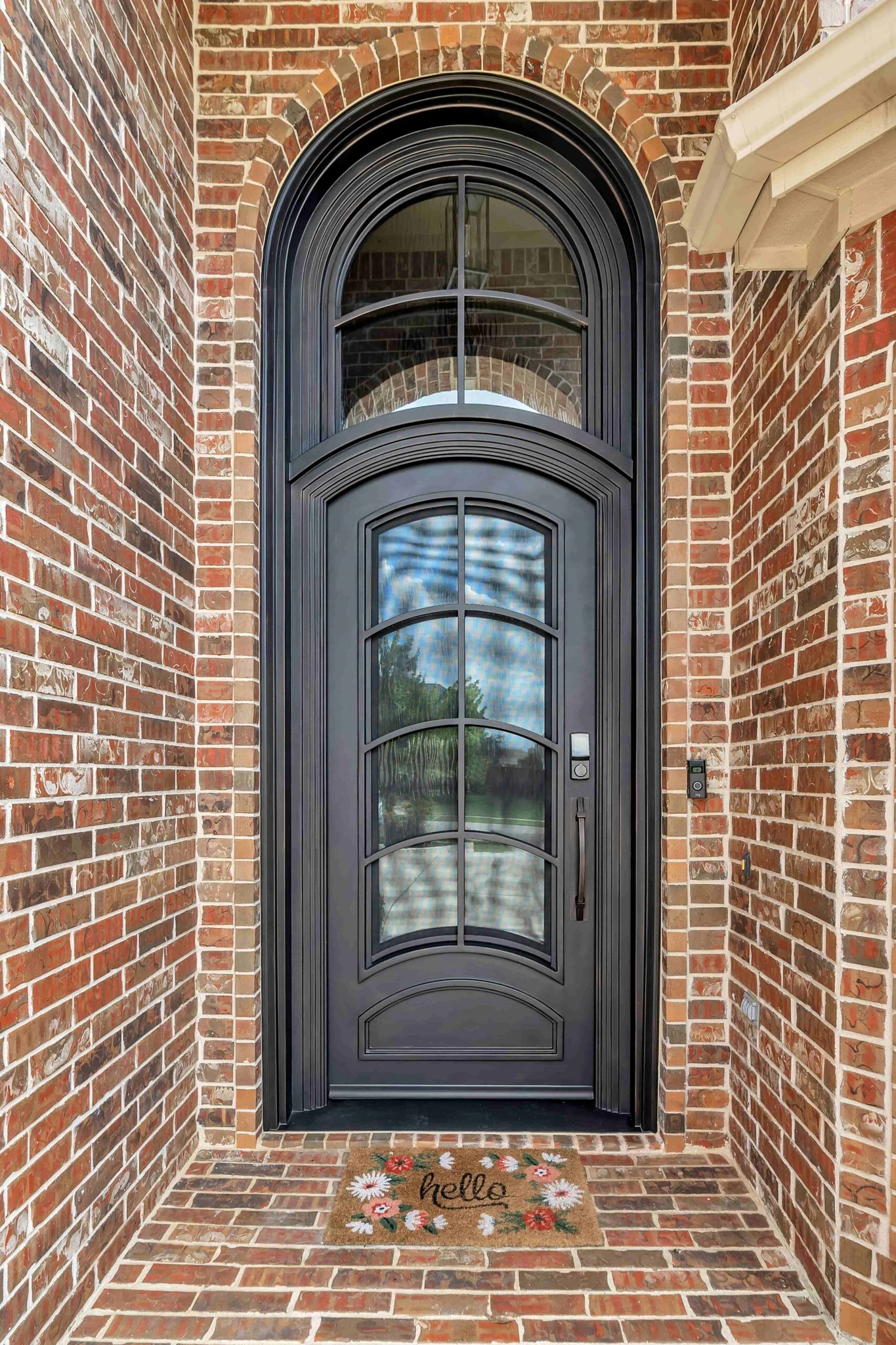 Modern black steel single arched entry door with grid glass, brick exterior