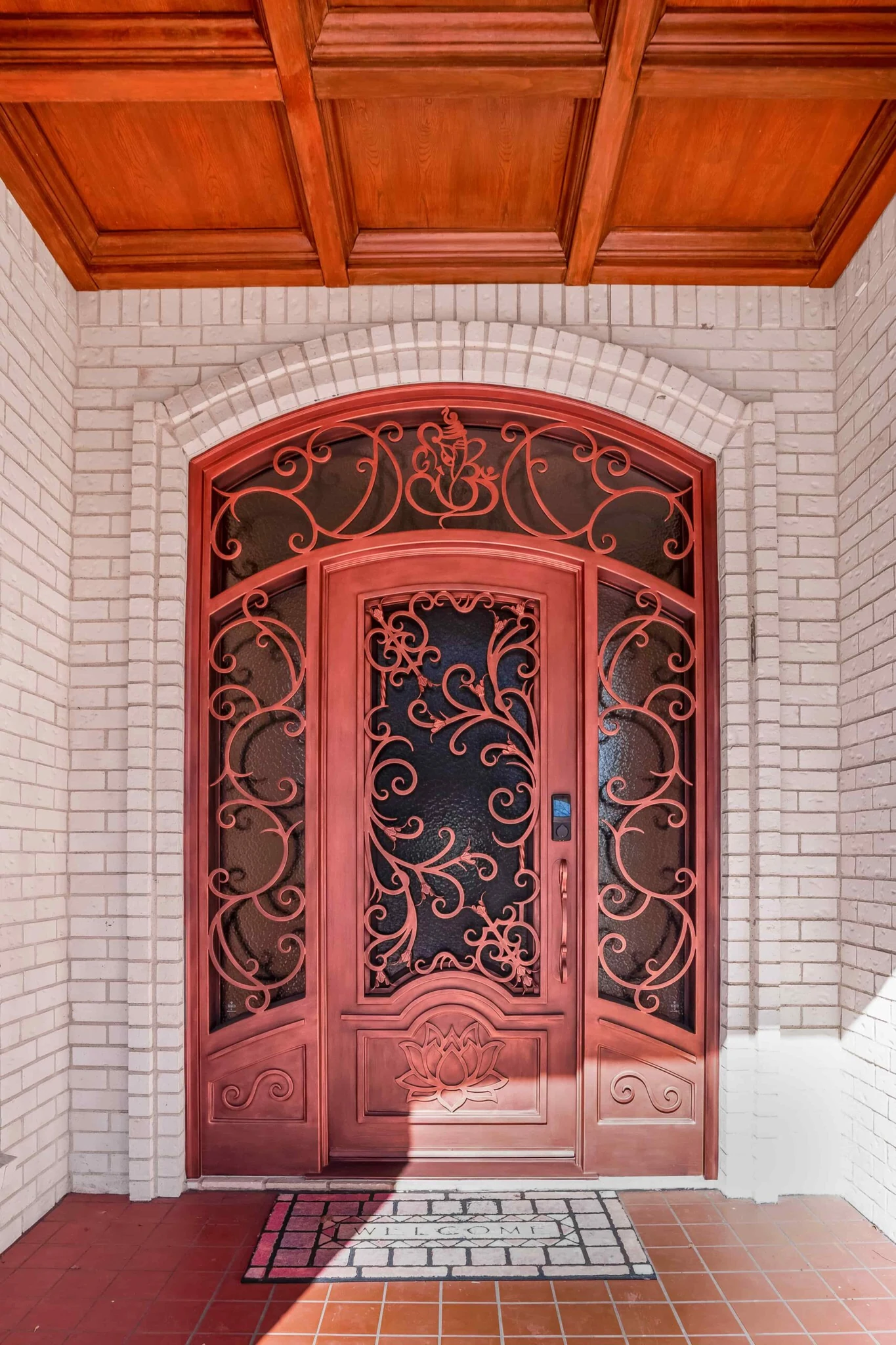 Red iron double arched entry door with scrollwork and textured glass, brick surround